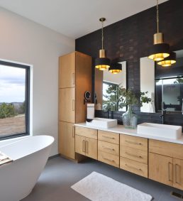 Luxury bathroom in a custom home built by Black Hills Homes in Frawley Ranch Estates in Spearfish, SD, featuring a freestanding tub with scenic views, double vanity, modern lighting, and natural wood cabinetry.