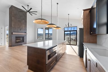 Modern kitchen and living area of a custom home built by Black Hills Homes in Spearfish, SD, featuring a large island, pendant lighting, floor-to-ceiling fireplace, and panoramic Black Hills views through oversized windows.